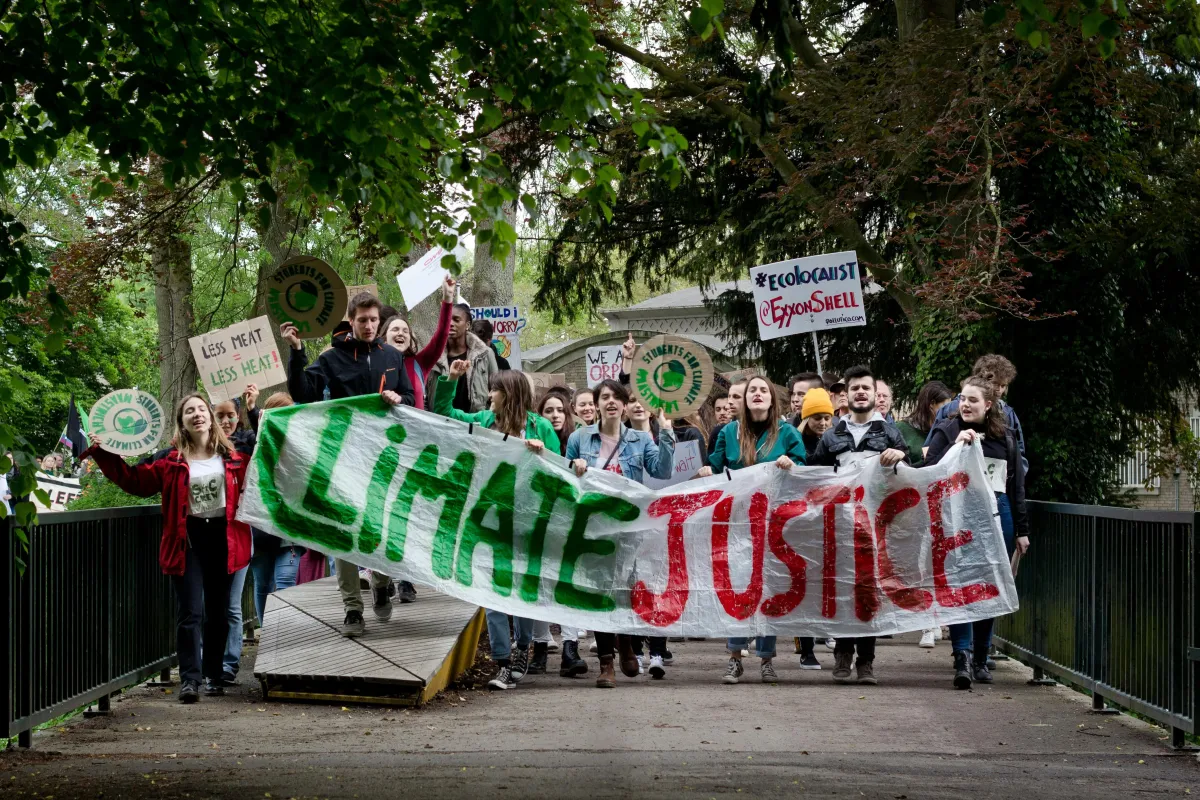 A crowd marching for climate justice carrying a green banner